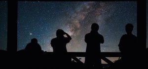 Four people stargazing silhouetted against the milky way
